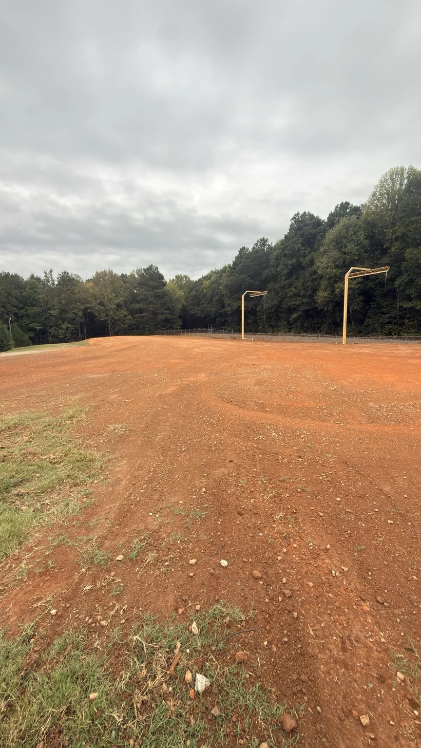Open, cleared red-clay industrial yard with utility poles and a wooded perimeter